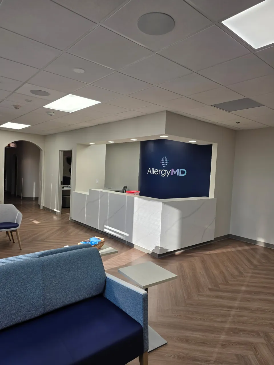 Completed medical office reception with quartz-clad desk, navy signage wall and herringbone vinyl plank flooring