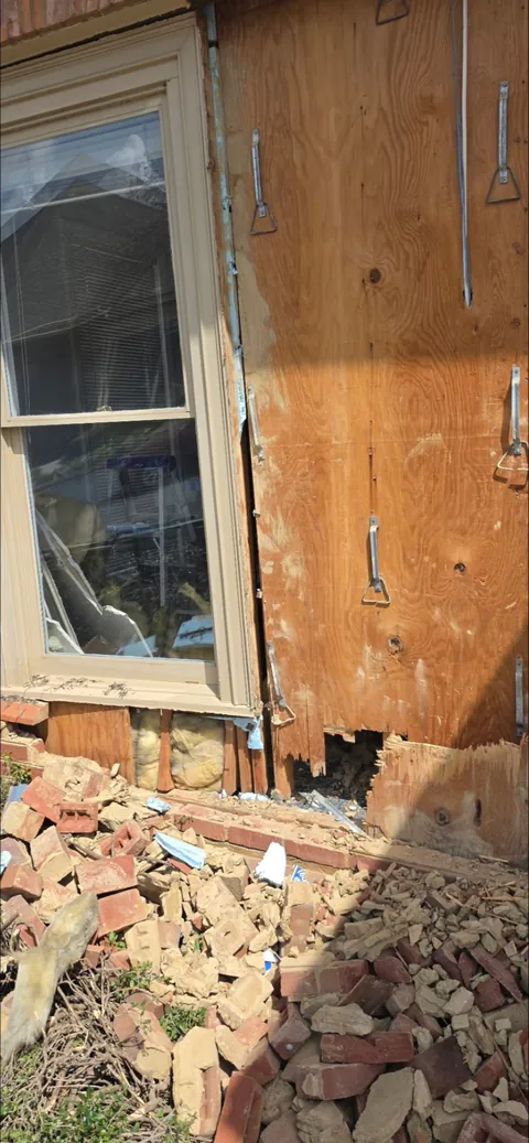 Close-up of collapsed brick veneer and damaged wall sheathing beside a window