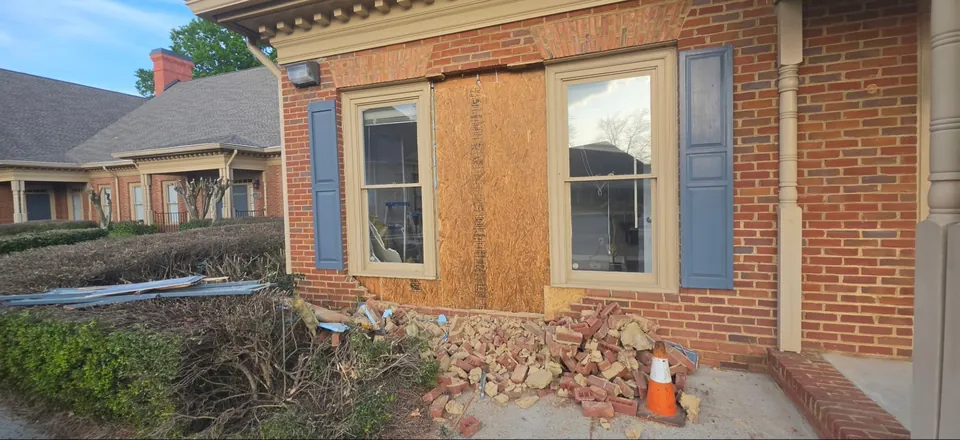 Damaged brick veneer wall boarded with plywood, with fallen brick on the walkway